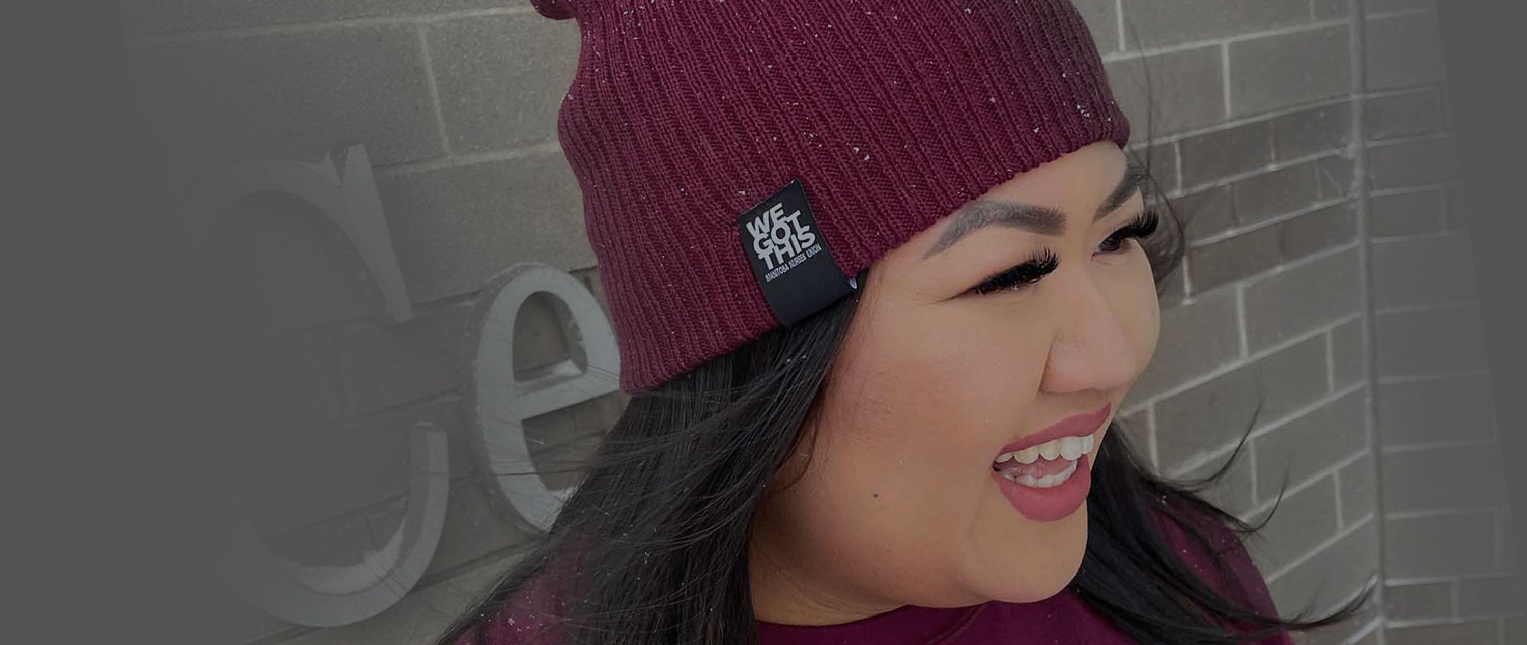 Smiling woman wearing a merlot coloured beanie toque with "We Got This" slogan on tag.